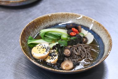 Tahta masadaki siyah tencerede tavuklu erişte. Japon eriştesi bok eriştesi çorbası mantarlı ve sebzeli siyah kase.