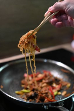 Şef tavada kızarmış erişte pişiriyor.