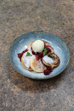 Üzerinde pudra şekeriyle toz haline getirilmiş, şerbetli kırmızı kirazlarla servis edilen, tüylü altın krep içeren güzel bir tatlı.