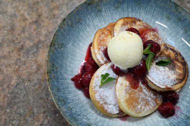 Üzerinde pudra şekeriyle toz haline getirilmiş, şerbetli kırmızı kirazlarla servis edilen, tüylü altın krep içeren güzel bir tatlı.