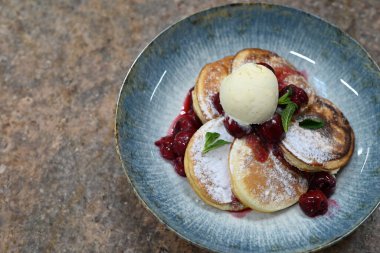 Üzerinde pudra şekeriyle toz haline getirilmiş, şerbetli kırmızı kirazlarla servis edilen, tüylü altın krep içeren güzel bir tatlı.