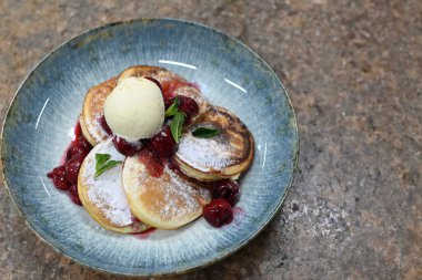 Üzerinde pudra şekeriyle toz haline getirilmiş, şerbetli kırmızı kirazlarla servis edilen, tüylü altın krep içeren güzel bir tatlı.
