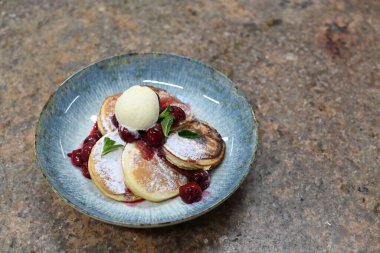Üzerinde pudra şekeriyle toz haline getirilmiş, şerbetli kırmızı kirazlarla servis edilen, tüylü altın krep içeren güzel bir tatlı.