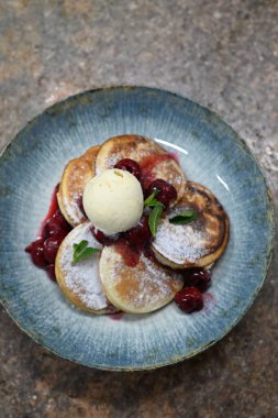 Üzerinde pudra şekeriyle toz haline getirilmiş, şerbetli kırmızı kirazlarla servis edilen, tüylü altın krep içeren güzel bir tatlı.