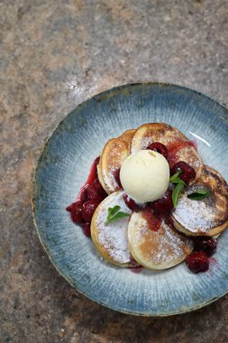Üzerinde pudra şekeriyle toz haline getirilmiş, şerbetli kırmızı kirazlarla servis edilen, tüylü altın krep içeren güzel bir tatlı.