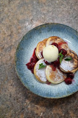 Üzerinde pudra şekeriyle toz haline getirilmiş, şerbetli kırmızı kirazlarla servis edilen, tüylü altın krep içeren güzel bir tatlı.