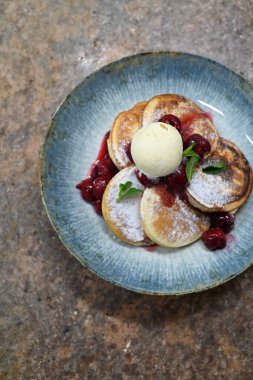 Üzerinde pudra şekeriyle toz haline getirilmiş, şerbetli kırmızı kirazlarla servis edilen, tüylü altın krep içeren güzel bir tatlı.
