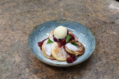 Üzerinde pudra şekeriyle toz haline getirilmiş, şerbetli kırmızı kirazlarla servis edilen, tüylü altın krep içeren güzel bir tatlı.