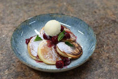 Üzerinde pudra şekeriyle toz haline getirilmiş, şerbetli kırmızı kirazlarla servis edilen, tüylü altın krep içeren güzel bir tatlı.