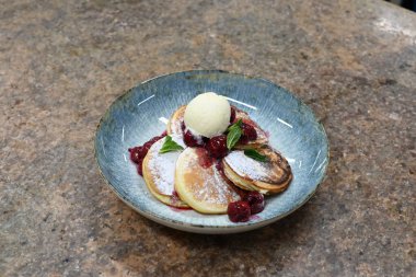 Üzerinde pudra şekeriyle toz haline getirilmiş, şerbetli kırmızı kirazlarla servis edilen, tüylü altın krep içeren güzel bir tatlı.