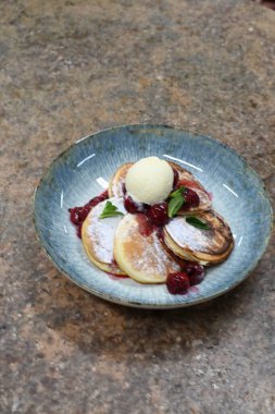 Üzerinde pudra şekeriyle toz haline getirilmiş, şerbetli kırmızı kirazlarla servis edilen, tüylü altın krep içeren güzel bir tatlı.