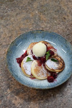 Üzerinde pudra şekeriyle toz haline getirilmiş, şerbetli kırmızı kirazlarla servis edilen, tüylü altın krep içeren güzel bir tatlı.