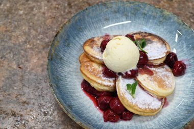 Üzerinde pudra şekeriyle toz haline getirilmiş, şerbetli kırmızı kirazlarla servis edilen, tüylü altın krep içeren güzel bir tatlı.