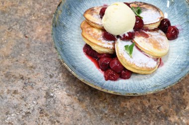 Üzerinde pudra şekeriyle toz haline getirilmiş, şerbetli kırmızı kirazlarla servis edilen, tüylü altın krep içeren güzel bir tatlı.