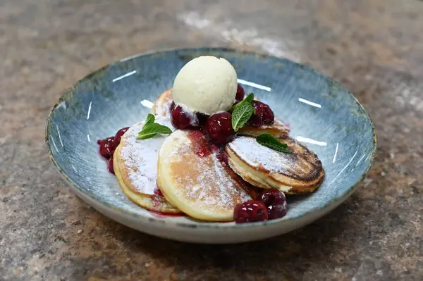 Üzerinde pudra şekeriyle toz haline getirilmiş, şerbetli kırmızı kirazlarla servis edilen, tüylü altın krep içeren güzel bir tatlı.