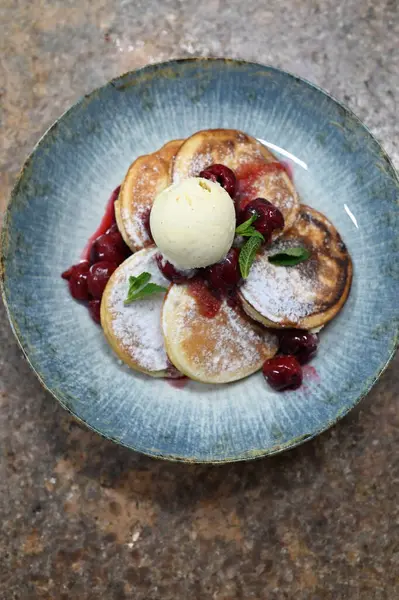 Üzerinde pudra şekeriyle toz haline getirilmiş, şerbetli kırmızı kirazlarla servis edilen, tüylü altın krep içeren güzel bir tatlı.