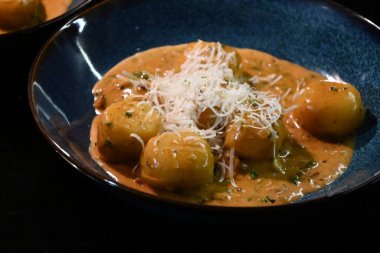 color photo of a dish of potato gnocchi sprinkled with parmesan, in a pepper sauce, with herbs, traditional homemade tasty food, close up view clipart