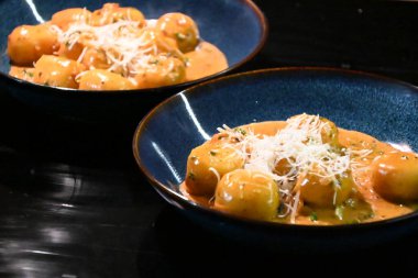 color photo of a dish of potato gnocchi sprinkled with parmesan, in a pepper sauce, with herbs, traditional homemade tasty food, close up view clipart