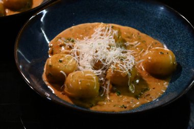 color photo of a dish of potato gnocchi sprinkled with parmesan, in a pepper sauce, with herbs, traditional homemade tasty food, close up view clipart