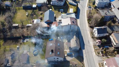 Baharın başlarında küçük bir Avrupa kasabasının havadan görünüşü, kalın beyaz duman yayan bir arka bahçe yangınını yakalıyor.