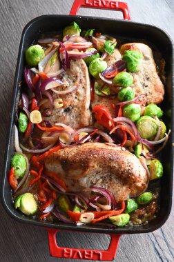 fırında tavuk göğsü ve brokolili kırmızı lahana ve siyah beton arka planda fırın kabında soğan. en üstteki görünüm.