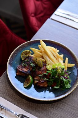 Restoranda sebzeli ızgara tavuk göğsü ve salata, masada patates kızartması ve taze sebzeyle servis ediliyor..