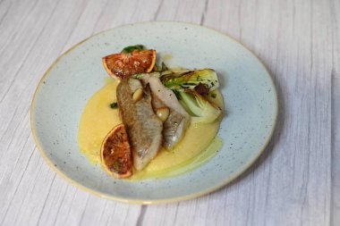 Koyu morina filetosu, kremalı polenta, kan portakalı segmentleri ve açık arkaplanda taze yeşil salata içeren güzel bir ev yapımı yemeğin üst görüntüsü.