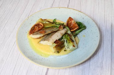 Koyu morina filetosu, kremalı polenta, kan portakalı segmentleri ve açık arkaplanda taze yeşil salata içeren güzel bir ev yapımı yemeğin üst görüntüsü.