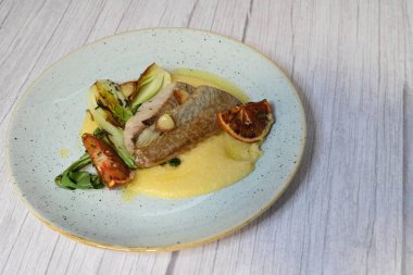Koyu morina filetosu, kremalı polenta, kan portakalı segmentleri ve açık arkaplanda taze yeşil salata içeren güzel bir ev yapımı yemeğin üst görüntüsü.