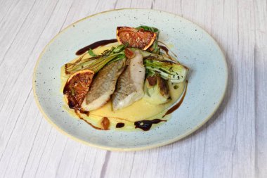 Koyu morina filetosu, kremalı polenta, kan portakalı segmentleri ve açık arkaplanda taze yeşil salata içeren güzel bir ev yapımı yemeğin üst görüntüsü.