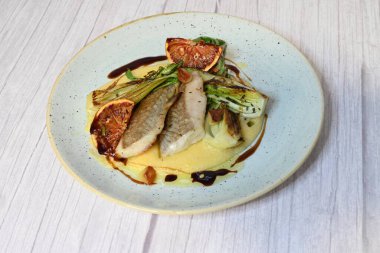 Koyu morina filetosu, kremalı polenta, kan portakalı segmentleri ve açık arkaplanda taze yeşil salata içeren güzel bir ev yapımı yemeğin üst görüntüsü.