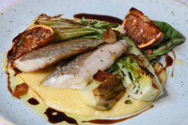 Koyu morina filetosu, kremalı polenta, kan portakalı segmentleri ve açık arkaplanda taze yeşil salata içeren güzel bir ev yapımı yemeğin üst görüntüsü.