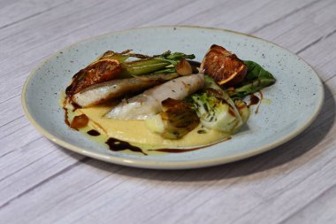 Koyu morina filetosu, kremalı polenta, kan portakalı segmentleri ve açık arkaplanda taze yeşil salata içeren güzel bir ev yapımı yemeğin üst görüntüsü.