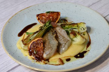 Koyu morina filetosu, kremalı polenta, kan portakalı segmentleri ve açık arkaplanda taze yeşil salata içeren güzel bir ev yapımı yemeğin üst görüntüsü.