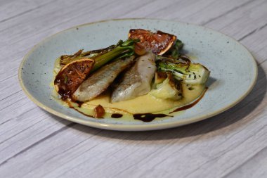 Koyu morina filetosu, kremalı polenta, kan portakalı segmentleri ve açık arkaplanda taze yeşil salata içeren güzel bir ev yapımı yemeğin üst görüntüsü.