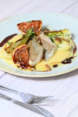 Koyu morina filetosu, kremalı polenta, kan portakalı segmentleri ve açık arkaplanda taze yeşil salata içeren güzel bir ev yapımı yemeğin üst görüntüsü.