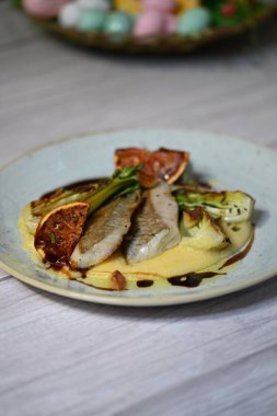 Koyu morina filetosu, kremalı polenta, kan portakalı segmentleri ve açık arkaplanda taze yeşil salata içeren güzel bir ev yapımı yemeğin üst görüntüsü.
