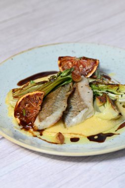 Koyu morina filetosu, kremalı polenta, kan portakalı segmentleri ve açık arkaplanda taze yeşil salata içeren güzel bir ev yapımı yemeğin üst görüntüsü.
