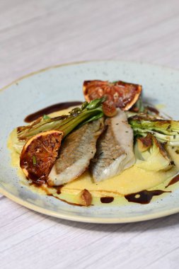 Koyu morina filetosu, kremalı polenta, kan portakalı segmentleri ve açık arkaplanda taze yeşil salata içeren güzel bir ev yapımı yemeğin üst görüntüsü.