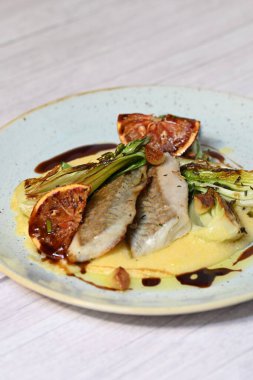 Koyu morina filetosu, kremalı polenta, kan portakalı segmentleri ve açık arkaplanda taze yeşil salata içeren güzel bir ev yapımı yemeğin üst görüntüsü.