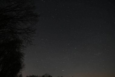 Yıldızlar arasında hızla ilerleyen parlak bir göktaşı içeren bahar gecesi gökyüzünün panoramik görüntüsü. 