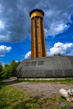 Arkasında parlak mavi bir gökyüzü olan tahta gözetleme kulesi. Çek kırsalının temiz ve açık atmosferine karşı geleneksel mimarinin çarpıcı bir örneği.