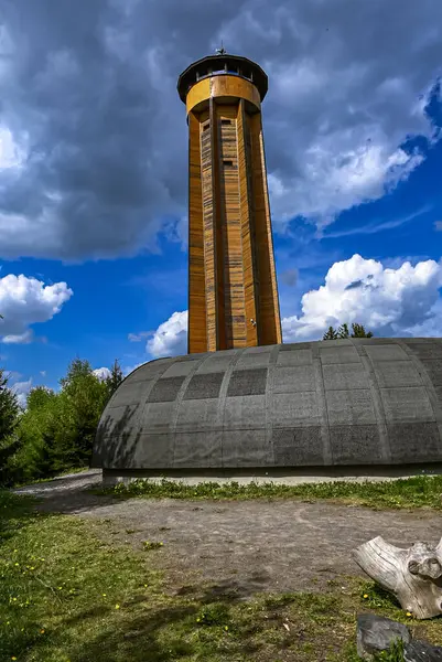Arkasında parlak mavi bir gökyüzü olan tahta gözetleme kulesi. Çek kırsalının temiz ve açık atmosferine karşı geleneksel mimarinin çarpıcı bir örneği.