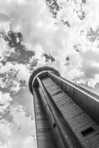 Çek Cumhuriyeti 'nin Kov hora tepesindeki baskın tahta gözetleme kulesinin etkileyici siyah beyaz manzarası. Güneşli bir günde dramatik bulutlarla yakalanan bu çarpıcı yapı zamansız tek renkli kırsal alana karşı duruyor..