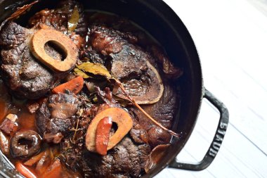 Kırmızı şarapla pişirilmiş kemikli yumuşak sığır eti, taze otlar ve tek bir kırsal siyah tencerede kök sebzelerle servis edilir. Zengin sos ve yavaş pişirilmiş malzemeler geleneksel bir konforlu yemek yemeğinin altını çiziyor..