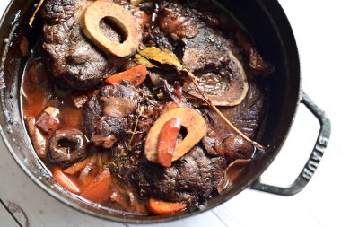 Kırmızı şarapla pişirilmiş kemikli yumuşak sığır eti, taze otlar ve tek bir kırsal siyah tencerede kök sebzelerle servis edilir. Zengin sos ve yavaş pişirilmiş malzemeler geleneksel bir konforlu yemek yemeğinin altını çiziyor..