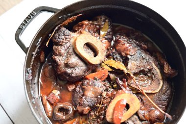 Kırmızı şarapla pişirilmiş kemikli yumuşak sığır eti, taze otlar ve tek bir kırsal siyah tencerede kök sebzelerle servis edilir. Zengin sos ve yavaş pişirilmiş malzemeler geleneksel bir konforlu yemek yemeğinin altını çiziyor..