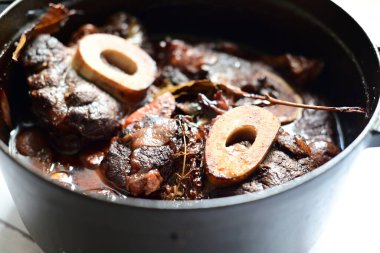 Kırmızı şarapla pişirilmiş kemikli yumuşak sığır eti, taze otlar ve tek bir kırsal siyah tencerede kök sebzelerle servis edilir. Zengin sos ve yavaş pişirilmiş malzemeler geleneksel bir konforlu yemek yemeğinin altını çiziyor..