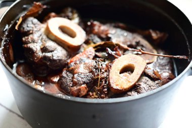 Kırmızı şarapla pişirilmiş kemikli yumuşak sığır eti, taze otlar ve tek bir kırsal siyah tencerede kök sebzelerle servis edilir. Zengin sos ve yavaş pişirilmiş malzemeler geleneksel bir konforlu yemek yemeğinin altını çiziyor..