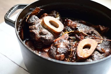 Kırmızı şarapla pişirilmiş kemikli yumuşak sığır eti, taze otlar ve tek bir kırsal siyah tencerede kök sebzelerle servis edilir. Zengin sos ve yavaş pişirilmiş malzemeler geleneksel bir konforlu yemek yemeğinin altını çiziyor..